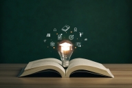 Open book with lightbulb sitting upright in spine area with bright mortar board inside; it is surrounded by floating slightly ghostly images of books, upward graphs, and other icons of education and work