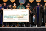 Professors in their ceremonial graduation garb holding a big check on a stage