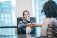 Young woman wearing headscarf shakes hands with another woman as if in an interview