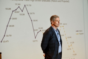 A man in front of a line graph trending downward.